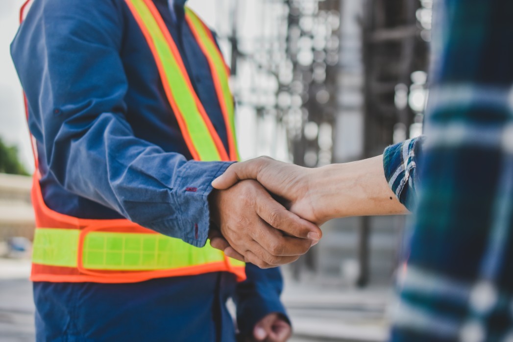 Worker in yellow safety vest shaking hands with a second worker.